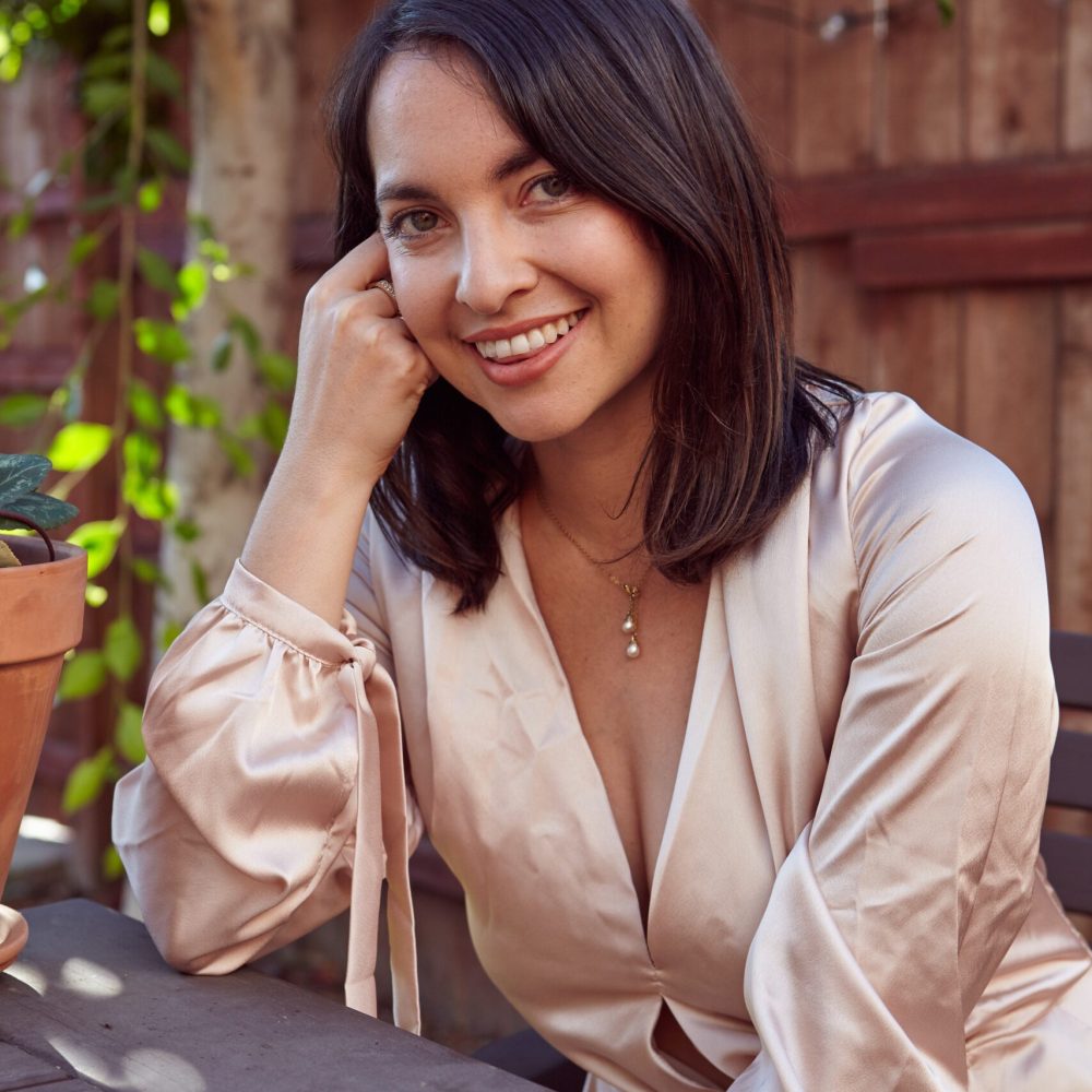 A vertical shot of a pretty female with a pink silk dress sitting in an outdoor cafe